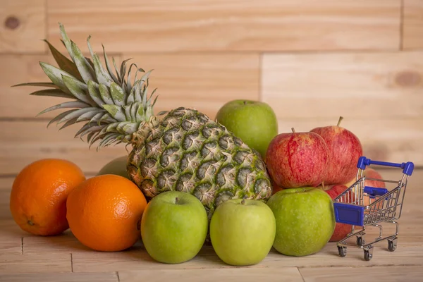 Mängd frukt och en liten kundvagn på en woden bord, studio — Stockfoto