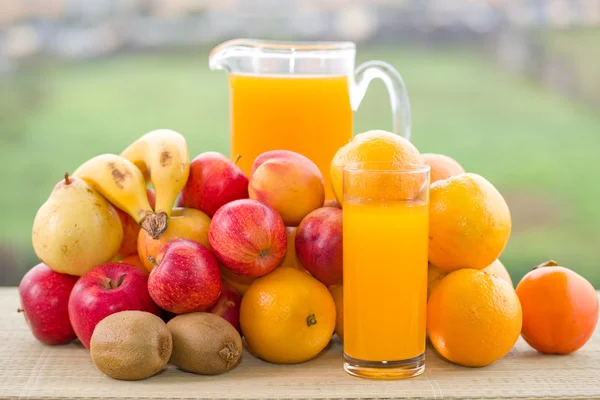 Glasses of orange juice and lots of fruits on wooden table outdoor — Stock Photo, Image