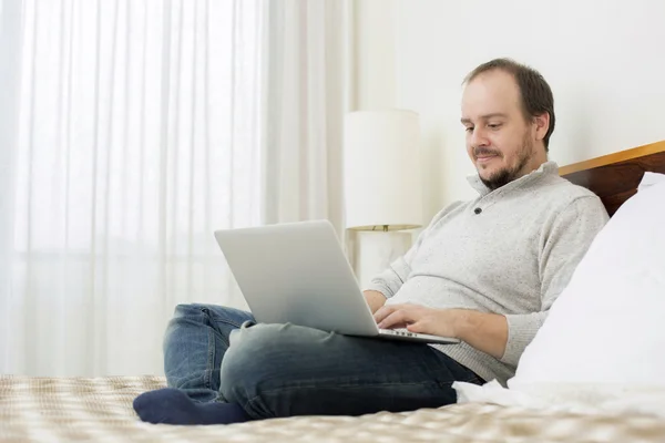 Uomo a letto che lavora con un computer portatile — Foto Stock