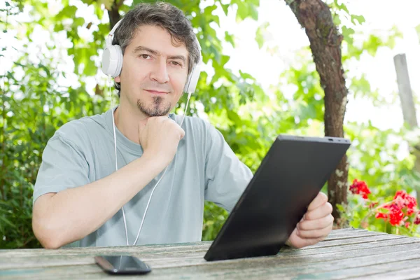 Mladý muž se tablet pc poslouchat hudbu se sluchátky — Stock fotografie