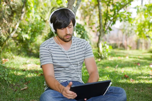 Junger Mann entspannt sich mit Tablet-PC und hört Musik mit Kopfhörern — Stockfoto