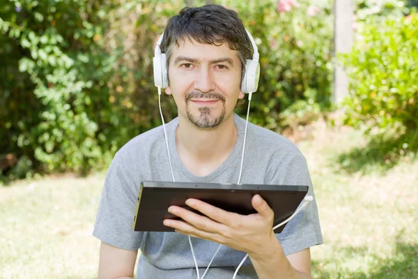 Jeune homme relaxant avec une tablette pc écouter de la musique avec des écouteurs — Photo