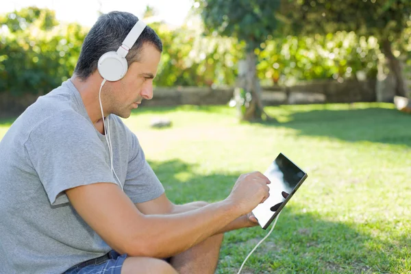 Giovane uomo che si rilassa con un tablet pc ascoltando musica con cuffie — Foto Stock