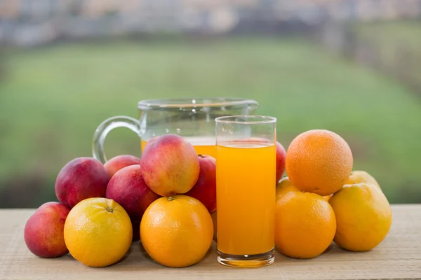 Стаканы апельсинового сока и много фруктов на деревянном столе на открытом воздухе — стоковое фото