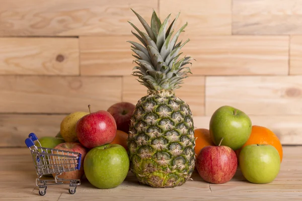 Mängd frukt och en liten kundvagn på ett träbord, studio bild — Stockfoto