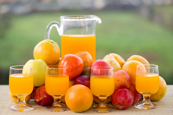 Vasos de jugo de naranja y muchas frutas en la mesa de madera al aire libre —  Fotos de Stock