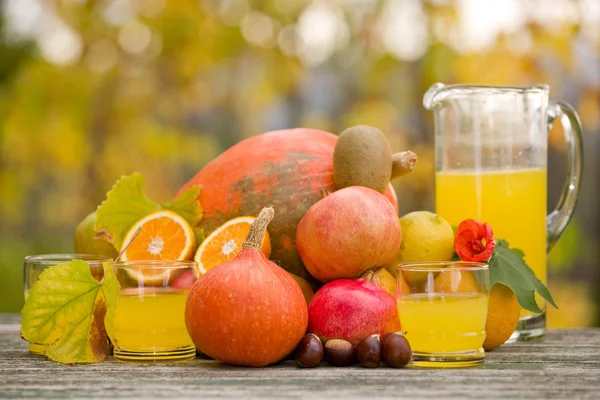 Saftgläser und jede Menge Herbstfrüchte auf Holztisch, draußen — Stockfoto