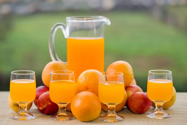 Glazen sinaasappelsap en een heleboel fruit op houten tafel buiten — Stockfoto