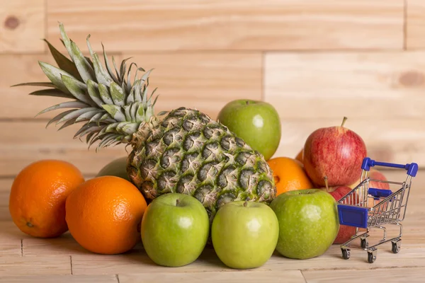 Mängd frukt och en liten kundvagn på ett träbord, studio bild — Stockfoto