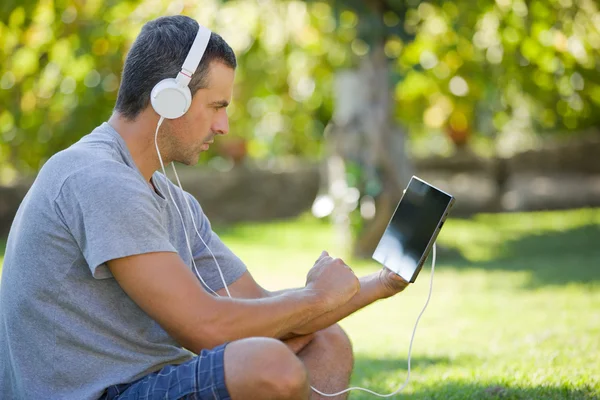 Giovane che si rilassa con un tablet pc ascoltando musica con le cuffie — Foto Stock