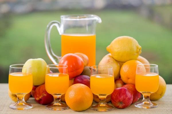 Vasos de jugo de naranja y muchas frutas en la mesa de madera al aire libre —  Fotos de Stock