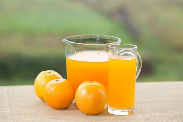 Vidro de delicioso suco de laranja e laranjas na mesa no jardim — Fotografia de Stock