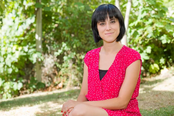 Joven mujer casual posando sentada, sonriendo a la cámara, al aire libre — Foto de Stock