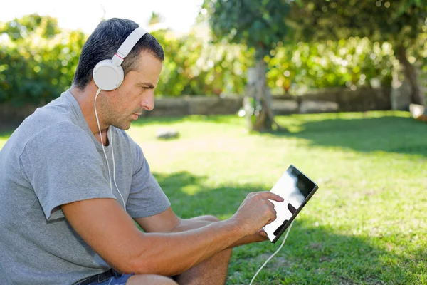 Giovane che si rilassa con un tablet pc ascoltando musica con le cuffie — Foto Stock