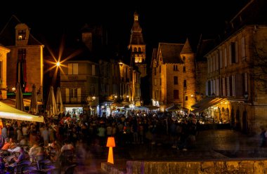 Sarlat-la-Caneda, Fransa: Aydınlatılmış taş binalar ve gece hayatının tadını çıkaran turist kalabalığıyla tarihi meydan manzarası.
