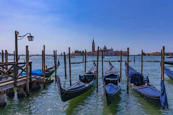 Venice, Italy: Gondolas docked at a wooden pier with calm waters, and a scenic view of Venetian architecture in the background.