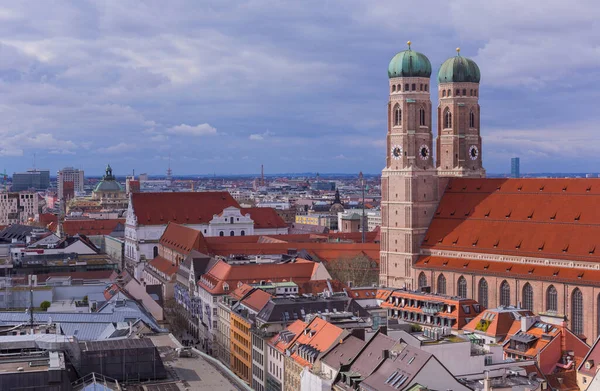 Münih, Almanya: Münih 'in panoramik manzarası Frauenkirche' nin kendine özgü yeşil kubbeli kuleleri, çeşitli binalarla çevrili, parçalı bulutlu bir gökyüzü altında kırmızı kiremitli çatıları var..