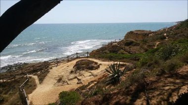 Atlantik kıyısının yukarısındaki kumtaşı ve sakin okyanusla güneşli uçurum manzarası. Albufeira, Portekiz