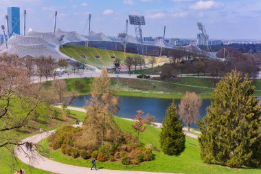 Münih, Almanya: Münih 'teki Olimpiyat manzarası, yemyeşil çimenler, ağaçlar ve Olimpiyat Stadyumu' nun ayırt edici mimarisi