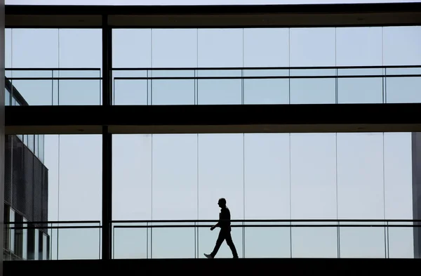 Vista silhueta de um jovem empresário caminhando em um prédio de escritórios moderno — Fotografia de Stock