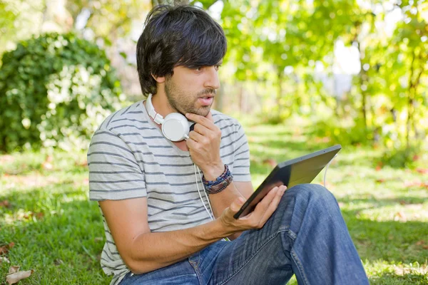 若い男にヘッドフォンで音楽を聴く、タブレット pc でリラックス、公園 — ストック写真