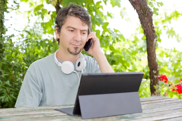 Giovane al telefono e tablet pc con cuffie, all'aperto — Foto Stock