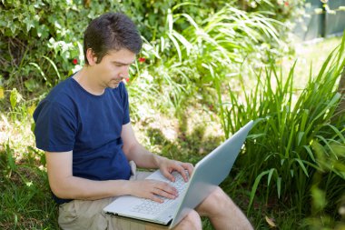 bir dizüstü bilgisayar ile çalışma çimenlerin üzerinde oturan adam