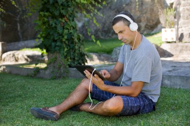 genç adam bir kulaklık ile müzik dinleme tablet pc ile rahatlatıcı bir parkta, açık