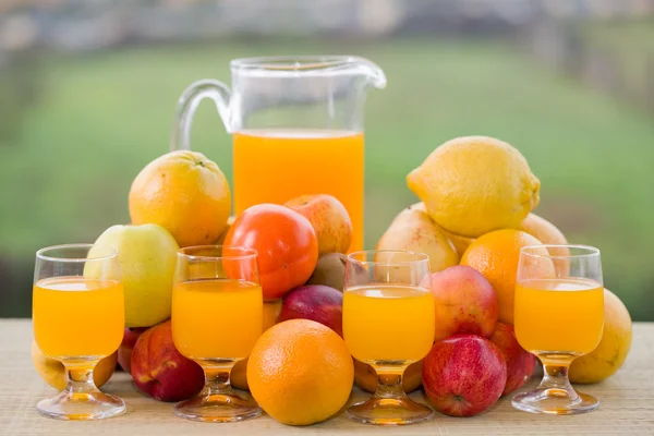 Vasos de jugo de naranja y muchas frutas en la mesa de madera al aire libre —  Fotos de Stock