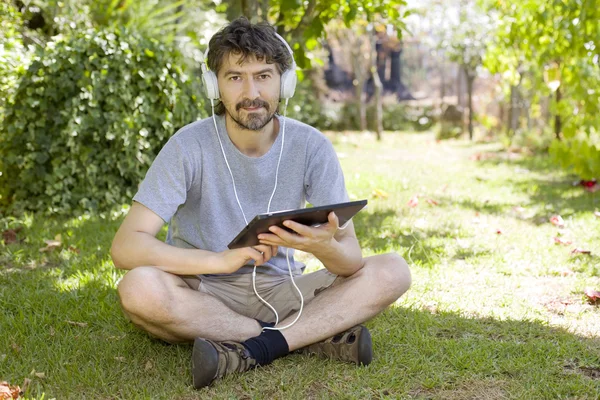 Jonge man met een tablet met koptelefoon, buiten — Stockfoto