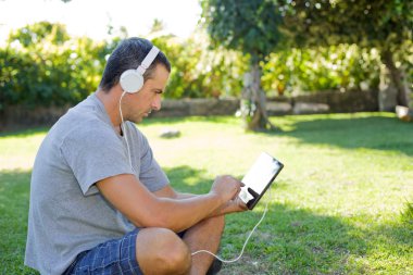 genç adam bir kulaklık ile müzik dinleme tablet pc ile rahatlatıcı bir parkta