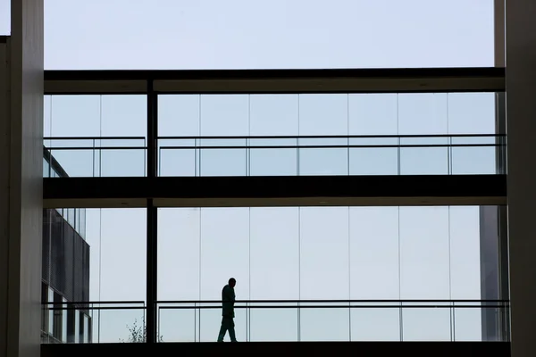 Silhouet weergave van jonge zakenman wandelen in modern kantoorgebouw interieur met panoramische ramen. — Stockfoto