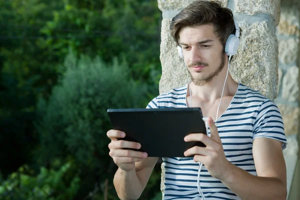 Uomo casual che tiene un tablet con cuffie, all'aperto — Foto Stock