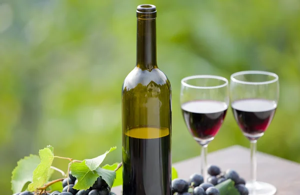 Wine bottle and grapes on wooden table outdoor — Stock Photo, Image