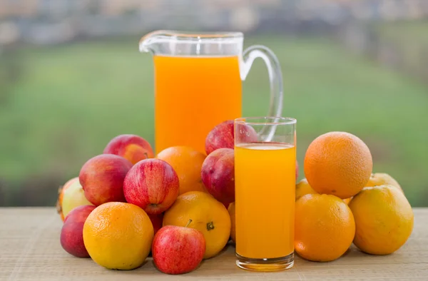 Orangensaft und viel Obst auf Holztisch im Freien — Stockfoto