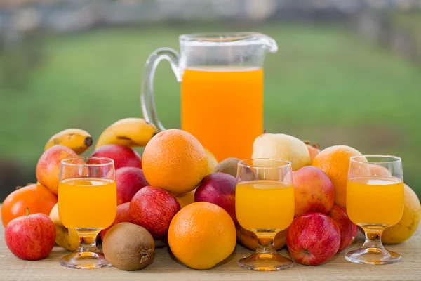 Orangensaft und viel Obst auf Holztisch im Freien — Stockfoto