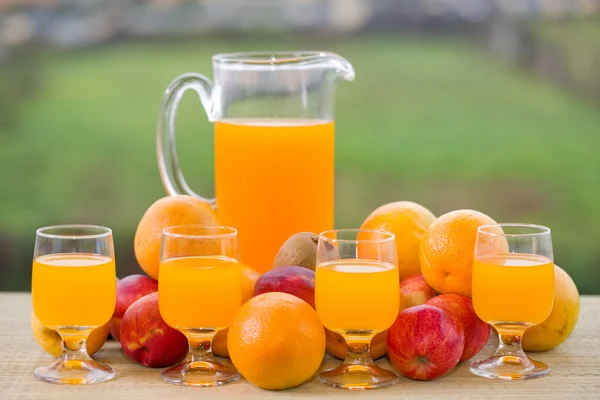 Стаканы апельсинового сока и много фруктов на деревянном столе на открытом воздухе — стоковое фото