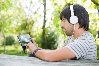 genç adam bir ahşap masa, açık bir kulaklık ile müzik dinleme tablet pc ile çalışma