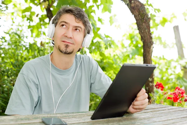 Młody mężczyzna pracujący z komputerem typu tablet z słuchawki, odkryty — Zdjęcie stockowe