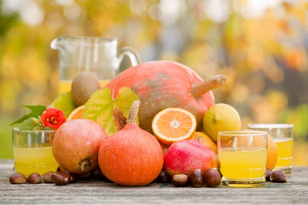 Saftgläser und jede Menge Herbstfrüchte auf Holztisch, draußen — Stockfoto
