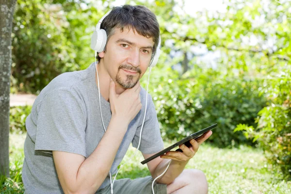 Jonge man met een tablet met koptelefoon, buiten — Stockfoto