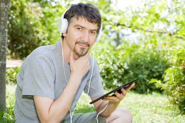 Giovane in possesso di un tablet con cuffie, all'aperto — Foto Stock