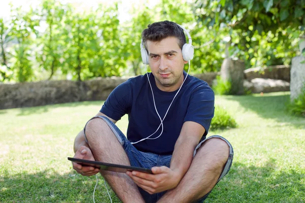 Jovem segurando um tablet com fones de ouvido, ao ar livre — Fotografia de Stock