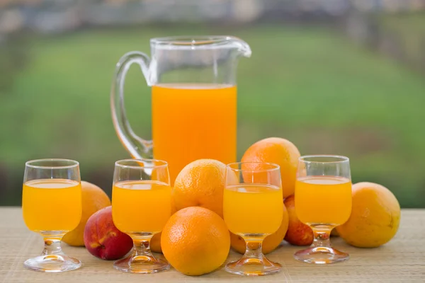 Vaso de delicioso jugo de naranja y naranjas en la mesa en el jardín —  Fotos de Stock