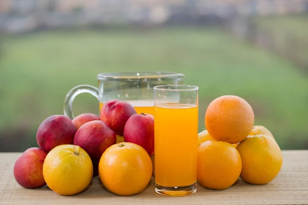 Orangensaft und viel Obst auf Holztisch im Freien — Stockfoto