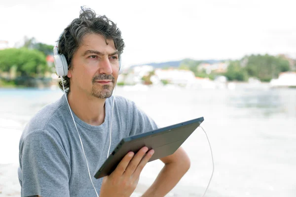 年轻男子手持戴着耳机，平板电脑在海滩 — 图库照片