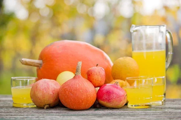 Saftgläser und jede Menge Herbstfrüchte auf Holztisch, draußen — Stockfoto