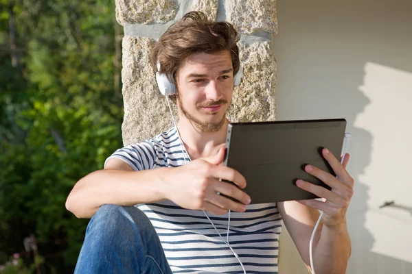 Giovane che si rilassa con un tablet pc ascoltando musica con cuffie, all'aperto — Foto Stock