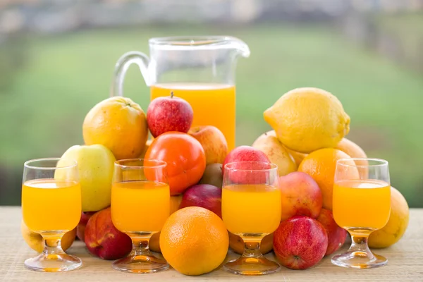 Glazen sinaasappelsap en een heleboel fruit op houten tafel buiten — Stockfoto