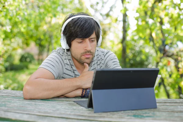 Молодой человек работает с планшетным компьютером, слушая музыку в наушниках — стоковое фото